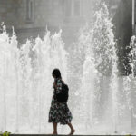 
              A woman walks past a fountain on a hot summer day in Berlin, Germany, Sunday, June 19, 2022. People flocked to parks and pools across Western Europe on Saturday for a bit of respite from an early heat wave. In Germany, where highs of 38 C (100.4 F) were expected, the health minister urged vulnerable groups to stay hydrated.(AP Photo/Markus Schreiber)
            