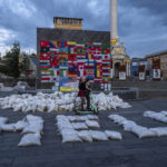 
              Women ride a scooter through Kyiv's Maidan Square, past sandbags that spell out 'HELP,' and flags displayed from around the world, in Ukraine, Saturday, June 25, 2022. (AP Photo/Nariman El-Mofty)
            