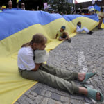 
              A girl sits on a huge Ukrainian flag during a demonstration against the war in Ukraine in Garmisch-Partenkirchen, Germany, on Sunday, June 26, 2022. The Group of Seven leading economic powers are meeting in Germany for their annual gathering Sunday through Tuesday. (AP Photo/Alexandra Beier)
            
