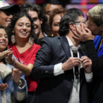 
              Veronica Alcocer kisses her husband, President elect Gustavo Petro, under the look of their daughters Antonella, left, and Sofia as they celebrate before supporters after he won a runoff presidential election in Bogota, Colombia, Sunday, June 19, 2022. (AP Photo/Fernando Vergara)
            