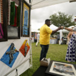 
              Local artist Patrick Henry greets a visitor near some of his paintings of pelicans for sale at the Bayou Boogaloo festival in New Orleans, Saturday, May 21, 2022. The large coastal birds were among the first species declared endangered in the U.S. in 1970. But a long-running effort to bring them back led to one of the country’s most inspiring comeback stories. (AP Photo/Gerald Herbert)
            