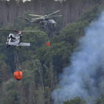 
              Helicopters carrying water to extinguish a wildfire in the area of the Ceske Svycarsko , Czech Switzerland, National Park, in Hrensko, Czech Republic, Wednesday, July 27, 2022.  (Ondrej Hajek/CTK via AP)
            