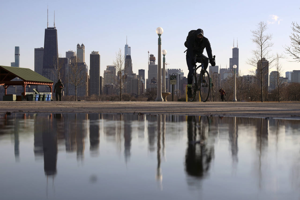 FILE - The Chicago skyline is reflected in the water of the thawed snow as a cyclist passes by at N...
