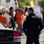 
              A Uvalde police officer watches as family and friends of those killed and injured in the school shootings at Robb Elementary take part in a protest march and rally, Sunday, July 10, 2022, in Uvalde, Texas. Families and residents are seeking answers and changes after the tragedy. (AP Photo/Eric Gay)
            