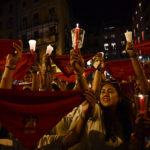 
              Revelers dressed in white and red color hold candles and kerchiefs as they sing San Fermin's song ''Pobre de Mi'' to close nine days of the running of the bulls, music and dance, at the San Fermin Festival, in Pamplona, northern Spain, early Friday, July 15, 2022. (AP Photo/Alvaro Barrientos)
            