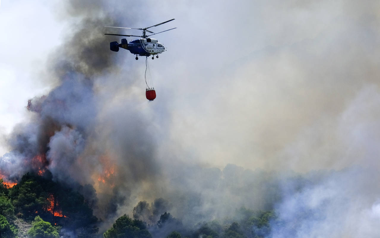 A helicopter launches water as a wildfire advances near a residential area in Alhaurin de la Torre,...