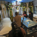 
              Relatives surround the coffins with the remains of Jair Valencia, Misael Olivares, and Yovani Valencia at their family house in San Marcos Atexquilapan, Veracruz state, Mexico, Wednesday, July 13, 2022. The three were among a group of migrants who died of heat and dehydration in a locked trailer-truck abandoned by smugglers on the outskirts of San Antonio, Texas, on June 27. (AP Photo/Felix Marquez)
            