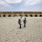 
              FILE - A woman and a boy walk on the dried up riverbed of the Zayandeh Roud river that no longer runs under the 400-year-old Si-o-seh Pol bridge, named for its 33 arches, in Isfahan, Iran on July 10, 2018. The Middle East is one of the most vulnerable regions in the world to the impact of climate change, and already the effects are being seen. This year's annual U.N. climate change conference, known as COP27, is being held in Egypt in November 2022, throwing a spotlight on the region. (AP Photo/Vahid Salemi, File)
            