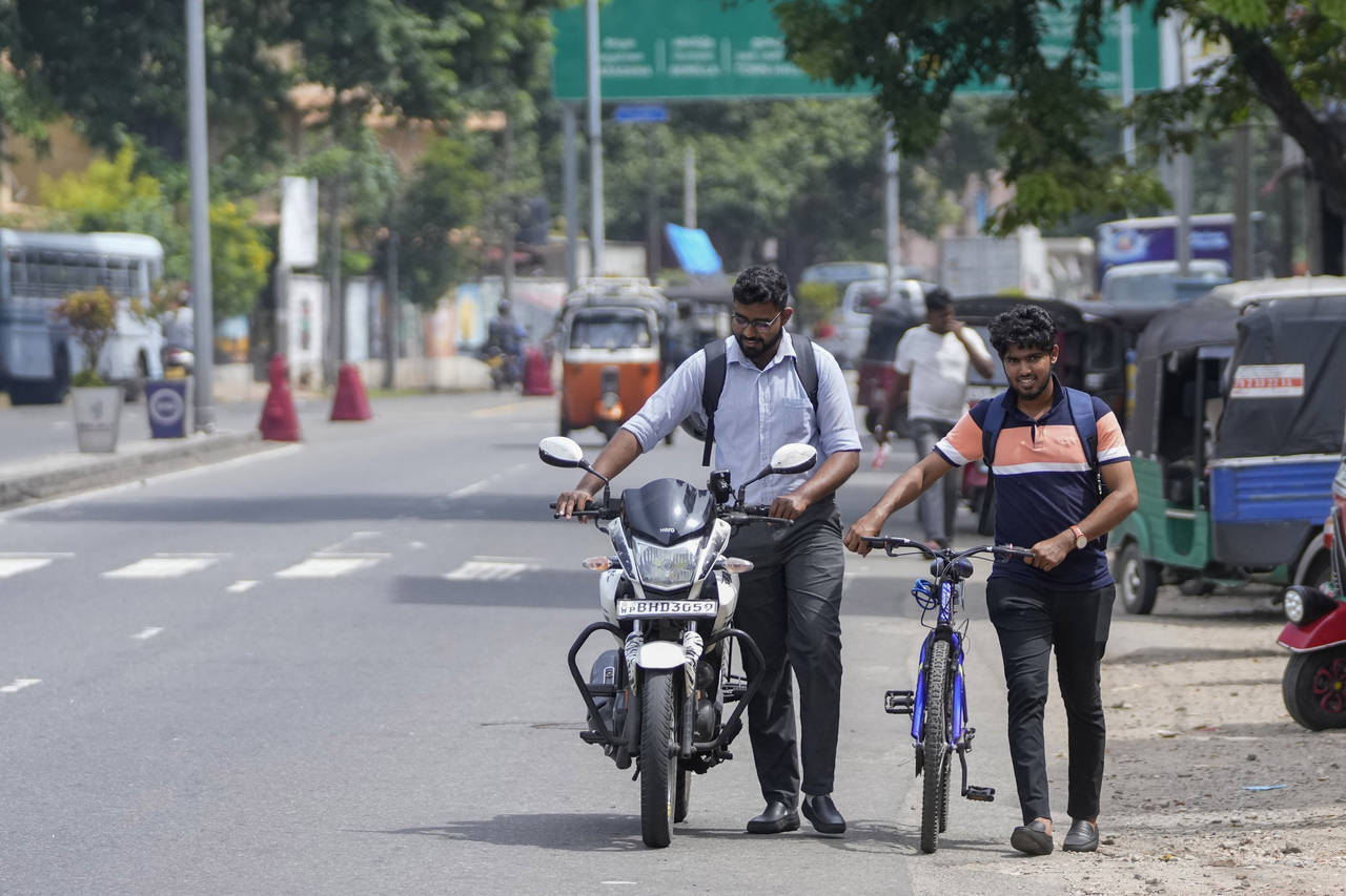 FILE- A motorist pushes his motorcycle along with a cyclist amid fuel shortage in Colombo, Sri Lank...