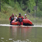
              FILE - Members of the Winchester, Ky., Fire Department walk inflatable boats across flood waters over a road in Jackson, Ky., to pick up people stranded by the floodwaters on Thursday, July 28, 2022. The same stubborn weather system caused intense downpours in St. Louis and Appalachia that led to devastating and in some cases deadly flooding. (AP Photo/Timothy D. Easley, File)
            
