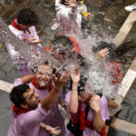 
              Water is thrown on revelers celebrating the launch of the 'Chupinazo' rocket, to mark the official opening of the 2022 San Fermin fiestas in Pamplona, Spain, Wednesday, July 6, 2022. The blast of a traditional firework opened Wednesday nine days of uninterrupted partying in Pamplona's famed running-of-the-bulls festival which was suspended for the past two years because of the coronavirus pandemic. (AP Photo/Alvaro Barrientos)
            