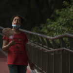 
              A woman wearing a face mask fans herself as she walks on a pedestrian bridge in Beijing, Tuesday, July 5, 2022. (AP Photo/Andy Wong)
            