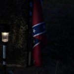 
              A small light illumines a confederate flag next to a grave on Thursday, June 23, 2022, in Athens, Ala., in the same cemetery David Guess was buried in March. David Guess was killed by gun violence. According to the police, Guess was shot with a handgun and burned in a wooded area with tires piled on his body and set on fire. (AP Photo/Brynn Anderson)
            