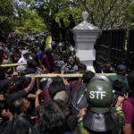 
              Protesters use an iron barricade to break the gate as they storm the compound of Sri Lankan Prime Minister Ranil Wickremesinghe's office, demanding he resign after president Gotabaya Rajapaksa fled the country amid economic crisis in Colombo, Sri Lanka, Wednesday, July 13, 2022. Sri Lanka’s president fled the country without stepping down Wednesday, plunging a country already reeling from economic chaos into more political turmoil. Protesters demanding a change in leadership then trained their ire on the prime minister and stormed his office. (AP Photo/Eranga Jayawardena)
            