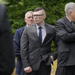 
              Volodymr Zhukovskyy, of West Springfield, Mass., center left, charged with negligent homicide in the deaths of seven motorcycle club members in a 2019 crash, is escorted by court security, behind left, and accompanied by defense attorney Steve Mirkin, right, while visiting the site of the crash on a two-lane highway, in Randolph, N.H., Monday, July 25, 2022. Zhukovskyy has pleaded not guilty to multiple counts of negligent homicide, manslaughter, reckless conduct and driving under the influence in the June 21, 2019, crash. Members of the jury visited the site for a viewing Monday. (AP Photo/Steven Senne, Pool)
            