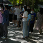 
              Residents stand underneath tree to avoid the hot sun as they line up for their routine coronavirus tests at a testing site in Beijing, Thursday, July 7, 2022. The Chinese capital has issued a mandate requiring people to show proof of COVID-19 vaccination before they can enter some public spaces including gyms, museums and libraries, drawing concern from city residents over the sudden policy announcement and its impact on their daily lives. (AP Photo/Andy Wong)
            