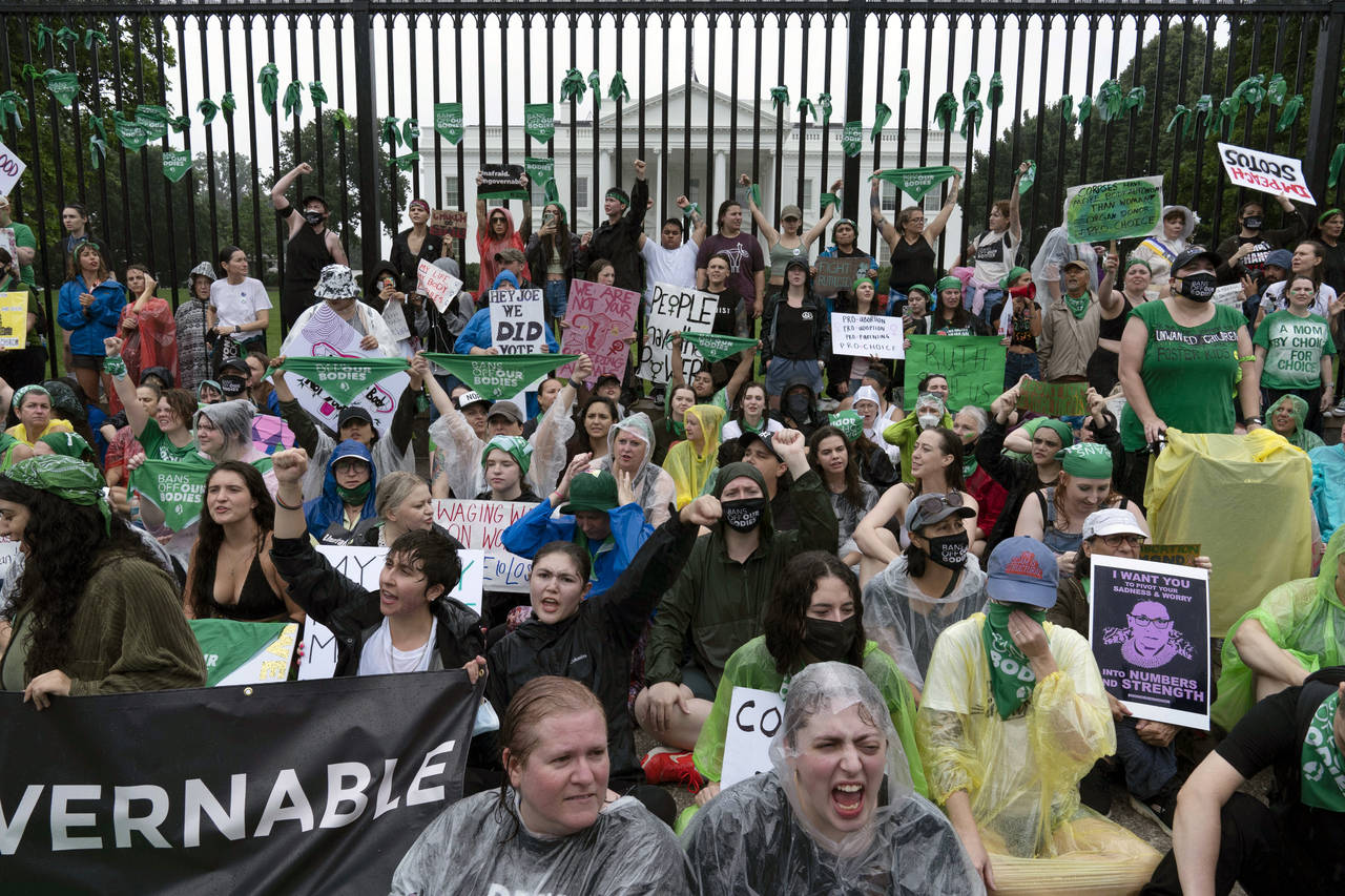 Abortion-rights demonstrators shout slogans after tying green flags to the fence of the White House...