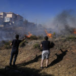 
              Residents spray water with a hose as fire burns near houses in the area of Drafi east of Athens on Wednesday, July 20, 2022. (AP Photo/Thanassis Stavrakis)
            