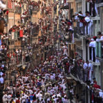 
              People watch from balconies as others run in the street with fighting bulls and steers during the running of the bulls at the San Fermin Festival in Pamplona, northern Spain, Saturday, July 9, 2022. Revellers from around the world flock to Pamplona every year for nine days of uninterrupted partying in Pamplona's famed running of the bulls festival which was suspended for the past two years because of the coronavirus pandemic. (AP Photo/Alvaro Barrientos)
            