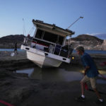 
              Craig Miller hauls a hose while trying to free his stranded houseboat at the Lake Mead National Recreation Area, Thursday, June 23, 2022, near Boulder City, Nev. Miller had been living on the stranded boat for over two weeks after engine trouble and falling lake levels left the boat above the water level. (AP Photo/John Locher)
            