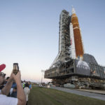 
              FILE - Invited guests and NASA employees take photos as NASA's Space Launch System (SLS) rocket with the Orion spacecraft aboard is rolled out of High Bay 3 of the Vehicle Assembly Building for the first time, at the Kennedy Space Center in Cape Canaveral, Fla., Thursday, March 17, 2022. On Wednesday, July 20, 2022, the 53rd anniversary of the Apollo 11 moon landing, NASA said it’s shooting for a late August test launch of its giant, new moon rocket. (Aubrey Gemignani/NASA via AP, File)
            