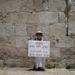 
              An activist with the Israeli movement Women Wage Peace holds a banner at a rally in front of Jerusalem's walled Old City calling on President Joe Biden to put peace between Israel and the Palestinians on the agenda, in Jerusalem, Thursday, July 14, 2022. Biden is in Israel for a three-day visit, his first as president. He will meet Israeli and Palestinian leaders before continuing on to Saudi Arabia. (AP Photo/Ariel Schalit)
            