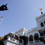 
              A Sri Lankan protester waves the national flag from the roof top of Sri Lankan Prime Minister Ranil Wickremesinghe's office, demanding he resign after president Gotabaya Rajapaksa fled the country amid economic crisis in Colombo, Sri Lanka, Wednesday, July 13, 2022. Rajapaksa fled on a military jet on Wednesday after angry protesters seized his home and office, and appointed Prime Minister Ranil Wickremesinghe as acting president while he is overseas. Wickremesinghe quickly declared a nationwide state of emergency to counter swelling protests over the country's economic and political collapse. (AP Photo/Eranga Jayawardena)
            
