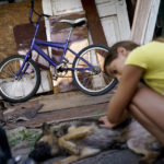 
              The bike belonging to Anastasiia Aleksandrova, 12, sits untouched as she pets her dog outside the home she shares with her grandparents in Sloviansk, Donetsk region, eastern Ukraine, Monday, Aug. 8, 2022. With no one her age left in her neighborhood and school classes taking place only online since Russia's invasion in February, games and social media on her smartphone have taken the place of the walks and bike rides she once enjoyed with the friends who have since fled to safety. (AP Photo/David Goldman)
            