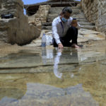 
              Syrian Christian Zuhair Al-Sahawi immerses his hand in water at the Bethany Beyond the Jordan baptismal site on the east bank of the Jordan River in Jordan on Wednesday, June 8, 2022. (AP Photo/Raad Adayleh)
            