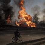 
              FILE - A man rides his bike past flames and smoke rising from a fire following a Russian attack in Kharkiv, Ukraine, March 25, 2022. Six months ago, Russian President Vladimir Putin sent troops into Ukraine in an unprovoked act of aggression, starting the largest military conflict in Europe since World War II. Putin expected a quick victory but it has turned into a grinding war of attrition. Russian offensive are largely stuck as Ukrainian forces increasingly target key facilities far behind the front lines. (AP Photo/Felipe Dana, File)
            