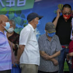 
              A man puts on his face mask as masked commuters wait for their buses at a stop in Beijing, Monday, Aug. 29, 2022. (AP Photo/Andy Wong)
            