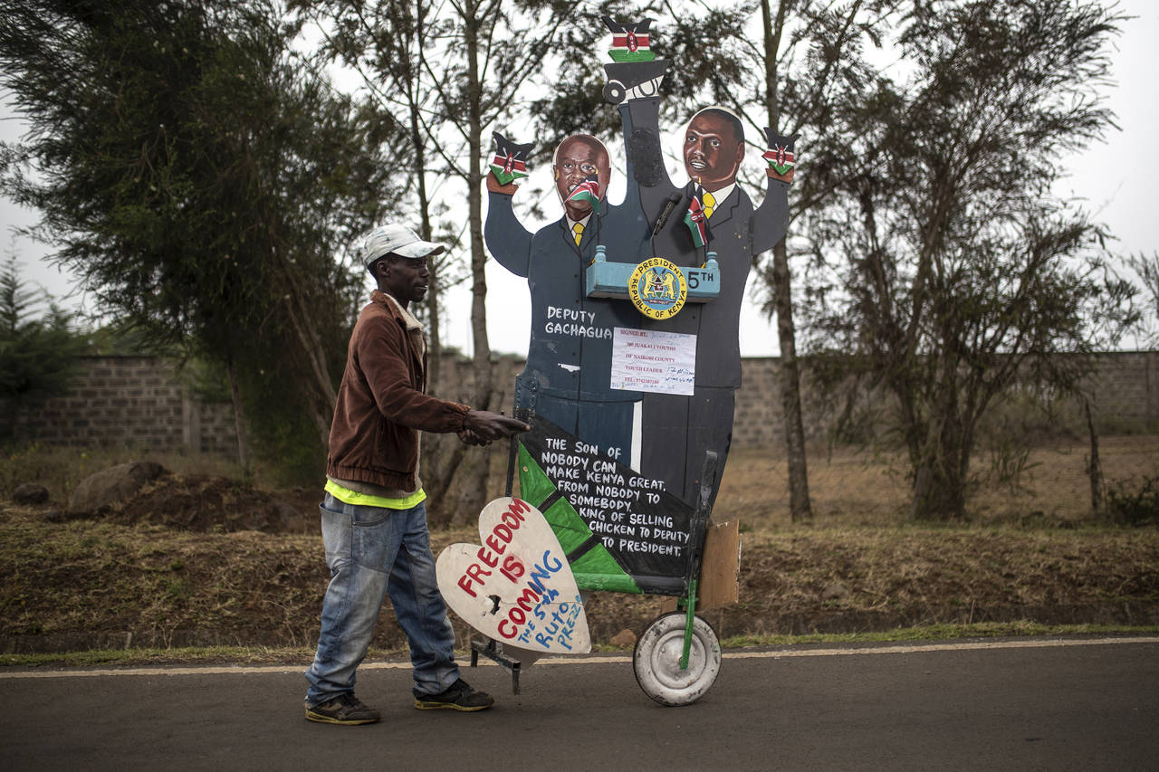 A supporter of Kenya's President-elect William Ruto pushes a cart with cardboard cutout of the pres...