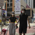 
              A couple wearing face masks walk along a street in Mongkok, a shopping district of Hong Kong, Monday, Aug. 8, 2022. Hong Kong will reduce the mandatory hotel quarantine for overseas arrivals to three days from a week, the city's leader said Monday. (AP Photo/Kin Cheung)
            