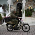 
              A man arrives on a small bike for the church service at a Greek Orthodox temple in Hasia, northwestern Athens, Greece, Sunday, Aug. 14, 2022. The Dormition of the Virgin Mary (or Mother of God as the Greeks usually refer to her) is celebrated on Aug. 15. The religious event is coupled with midsummer festivities, known as Panigiria, that often last more than a day with music, culinary feasts and, in many cases, flea markets. (AP Photo/Thanassis Stavrakis)
            
