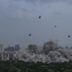 
              Cloud of dust rises as twin high-rise apartment towers are leveled to the ground in a controlled demolition in Noida, outskirts of New Delhi, India, Sunday, Aug. 28, 2022. The demolition was done after the country's top court declared them illegal for violating building norms. The 32-story and 29-story towers, constructed by a private builder were yet to be occupied and became India's tallest structures to be razed to the ground. (AP Photo/Altaf Qadri)
            