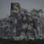 
              Cloud of dust rises as twin high-rise apartment towers are razed to ground in Noida, outskirts of New Delhi, India, Sunday, Aug. 28, 2022. The demolition was done after the country's top court declared them illegal for violating building norms. The 32-story and 29-story towers, constructed by a private builder were yet to be occupied and became India's tallest structures to be razed to the ground. (AP Photo/Altaf Qadri)
            