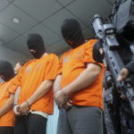 
              A police officer escorts suspects detained for drugs charges during a news conference in Bali, Indonesia on Friday, Aug. 5, 2022. Authorities in Indonesia arrested three foreigners, for distributing cocaine on the Indonesian resort island of Bali at the end of July. From the three suspects that are identified as British, Brazilian and Mexican, the officers from the National Narcotics Agency seized 844.59 gram (1.86 pounds) of cocaine with other drugs, including MDMA and marijuana. (AP Photo/Firdia Lisnawati)
            