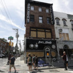 
              Pedestrians stop to look at the boarded-up Jim's Steaks and closed Eye's Gallery along South Street, Sunday, July 31, 2022, following a fire in Philadelphia. An electrical malfunction sparked a fast-moving fire that damaged one of Philadelphia’s best-known cheesesteak shops last week, authorities said. (Yong Kim/The Philadelphia Inquirer via AP)
            