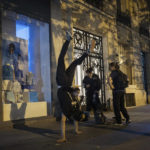 
              Hadj Benhalima from the collective "On the Spot" makes a headstand during a night of action where they will attempt to extinguish the lights of dozens of storefronts in Paris, Friday, July 29, 2022. (AP Photo/Lewis Joly)
            