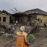 
              An elderly worker arrives with a broom at a crater caused by a rocket strike on a house in Kramatorsk, Donetsk region, eastern Ukraine, Friday, Aug. 12, 2022. There were no injuries reported in the strike. (AP Photo/David Goldman)
            