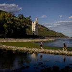 
              People walk over a stone dam, that is normally covered by water, towards the "Maeuseturm" (mice tower) in the middle of the river Rhine in Bingen, Germany, Friday, Aug. 12, 2022. The Rhine carries low water after a long drought period. (AP Photo/Michael Probst)
            