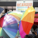 
              FILE - A sign-carrying anti-gay protester is surrounded by a sea of Pride umbrellas during the Pride parade in Winston-Salem, N.C., June 18, 2022. Hateful references to gays, lesbians and other LGBTQ Americans on social media surged following Florida's adoption of a law restricting how teachers can talk about sexual orientation with younger students. (AP Photo/Skip Foreman, File)
            
