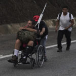 
              FILE - Venezuelan migrant Jesus Gonzalez, who broke his leg while crossing the Darien jungle, is pushed in a wheelchair along the Huehuetan highway in the state of Chiapas, Mexico, June 7, 2022. The 53-year-old man alternated between crutches and a wheelchair pushed by relatives and friends as the family continued northward to the U.S.-Mexico border. (AP Photo/Marco Ugarte, File)
            
