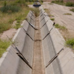 
              A dry irrigation canal runs between fields Thursday, Aug. 18, 2022, in Maricopa, Ariz. Kelly Anderson grows specialty crops for the flower industry and leases land to alfalfa farmers whose crops feed cattle at nearby dairy farms. He knows what's at stake as states dither over cuts and expects about half of the area will go unplanted next year, after farmers in the region lose all access to the river. (AP Photo/Matt York)
            