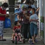 
              A woman puts on her face mask after getting her routine COVID-19 throat swabs with children at a coronavirus testing site outside a residential complex in Beijing, Monday, Aug. 29, 2022. (AP Photo/Andy Wong)
            