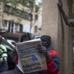 
              People discuss the election as a man reads a newspaper in Nairobi, Kenya, Friday, Aug. 12, 2022. Vote-tallying in Kenya's close presidential election isn't moving fast enough, the electoral commission chair said Friday, while parallel counting by local media dramatically slowed amid concerns about censorship or meddling. (AP Photo/Mosa'ab Elshamy)
            