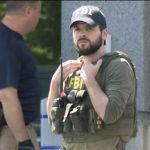 
              In this still image taken from WKEF/WRGT video, an FBI agent stands guard as members of the FBI Evidence Response Team work outside the FBI building in Kenwood, Ohio, Thursday, Aug. 11, 2022. An armed man decked out in body armor tried to breach a security screening area at an FBI field office in Ohio on Thursday, then fled and was injured in an exchange of gunfire in a standoff with law enforcement, authorities said. (Courtesy WKEF/WRGT via AP)
            