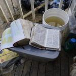 
              Kirsten Gomez brought out her English and Spanish Bibles to "read as they clean and start to repair their life," said Gomez, on Tuesday, Aug. 2, 2022, in Hindman, Ky., after massive flooding destroyed their home and cars. (AP Photo/Brynn Anderson)
            