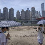 
              Students carrying umbrellas stand on the dry riverbed of the Jialing River in southwestern China's Chongqing Municipality, Friday, Aug. 19, 2022. Ships crept down the middle of the Yangtze on Friday after the driest summer in six decades left one of the mightiest rivers shrunk to barely half its normal width and set off a scramble to contain damage to a weak economy in a politically sensitive year. (AP Photo/Mark Schiefelbein)
            