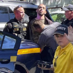 
              ADDS NAME OF DETAINED PERSON Law enforcement officers detain Hadi Matar, 24, of Fairview, N.J., outside the Chautauqua Institution, Friday, Aug. 12, 2022, in Chautauqua, N.Y.. Salman Rushdie, the author whose writing led to death threats from Iran in the 1980s, was attacked and apparently stabbed in the neck Friday by Matar who rushed the stage as he was about to give a lecture at the institute in western New York. (Charles Fox via AP)
            